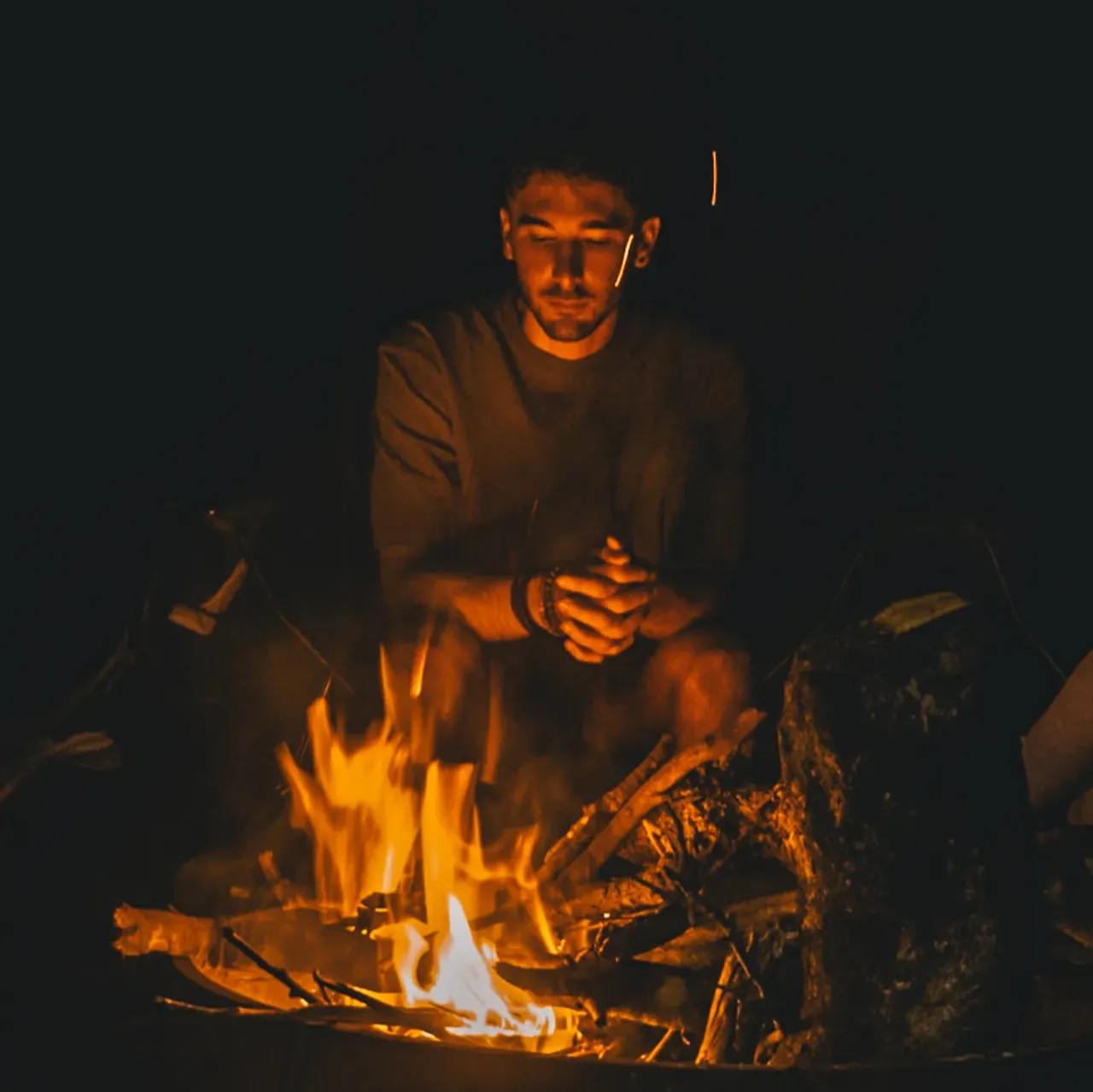 Romain Gal, fondateur du Cocon, assis près du feu de camp à la nuit tombée